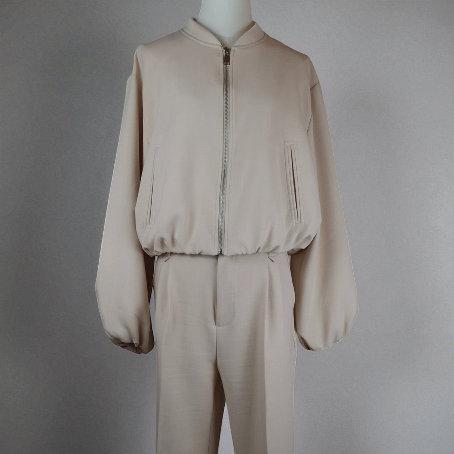 La Vie Continue beige polyester blend bomber jacket and high-waisted trousers set. The jacket has a zip closure and blousant effect. The trousers are straight-leg with front pleats.