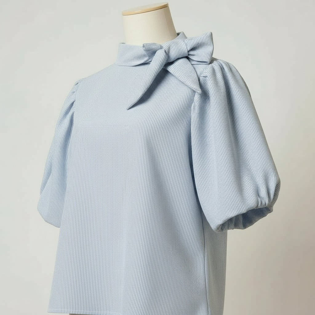 La Vie Continue light blue striped cotton-blend blouse with puffed short sleeves and a bow tie neck.