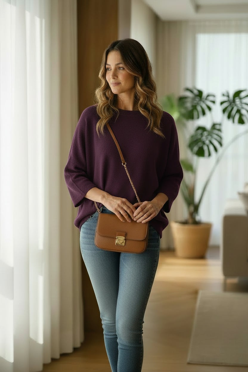 La Vie Continue plum purple relaxed fit sweater with wide sleeves and round neck, paired with blue jeans and a tan crossbody bag.