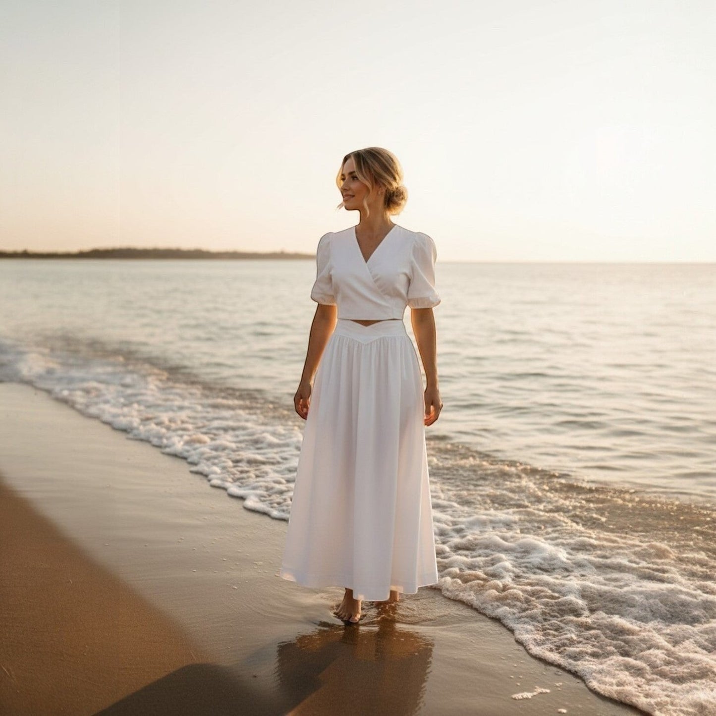 La Vie Continue white polyester wrap crop top and long skirt set on a woman walking on the beach at sunset.